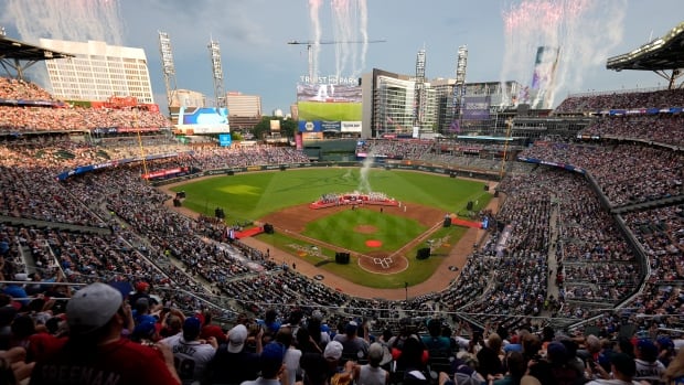 Long view of a baseball field, with teams on the diamond and what appears to be fireworks going off.