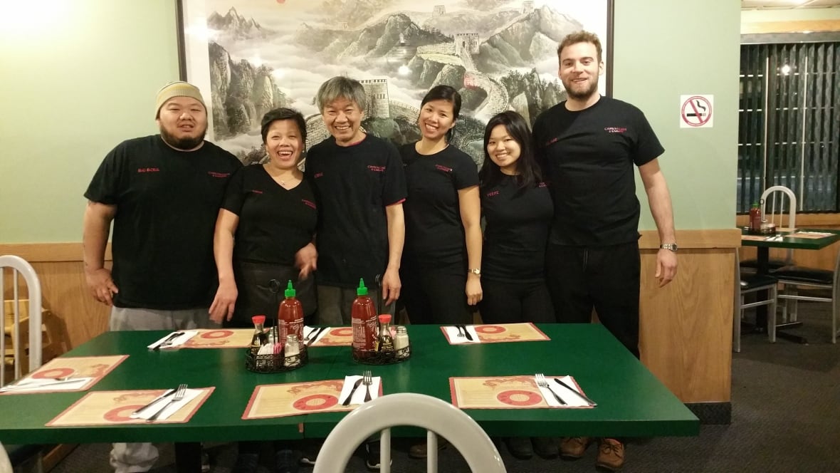 Three smiling women and three smiling men pose for a photo in front of a green restaurant table with placemats and cutlery laid out.