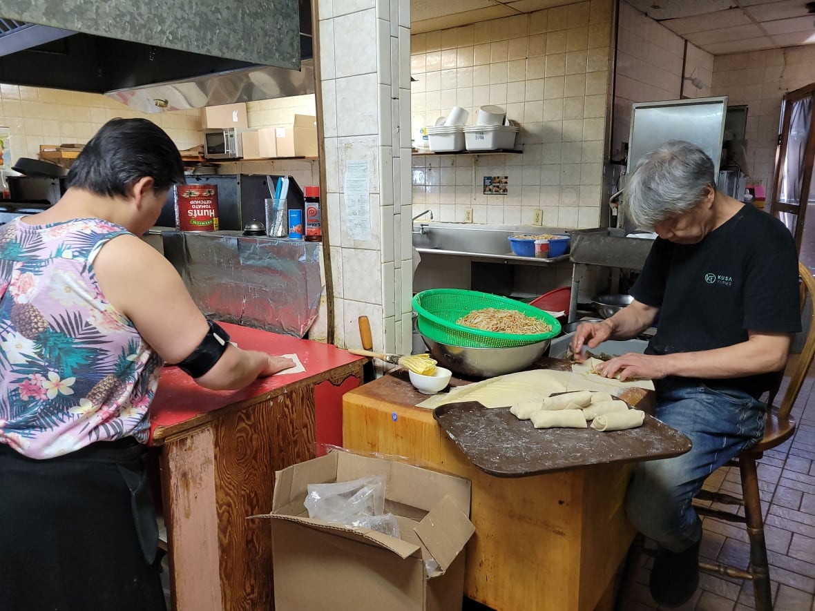 A man and a woman work beside each other rolling egg rolls inside a kitchen. 