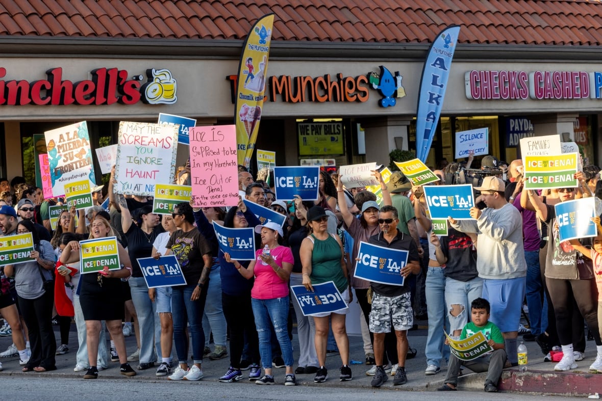 Dozens of people hold up signs on the sidewalk in an apparent protest. 