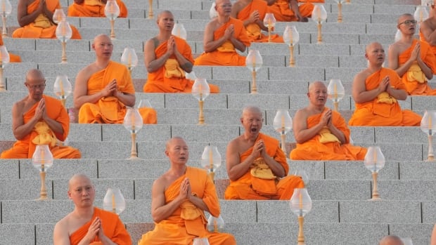 Monks in orange robes sit in prayer along steps