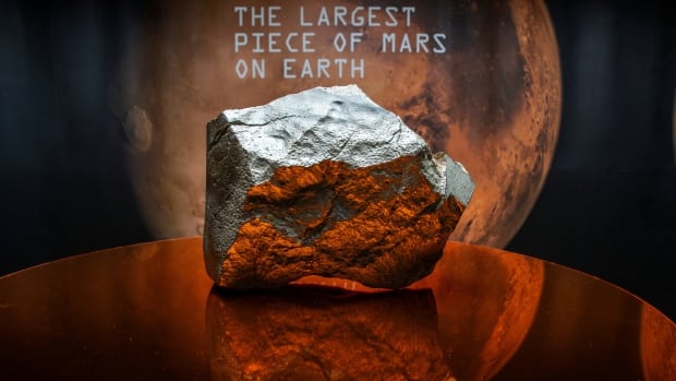 A large rock sits on a stand in front of a display that reads, "The largest piece of Mars on Earth."