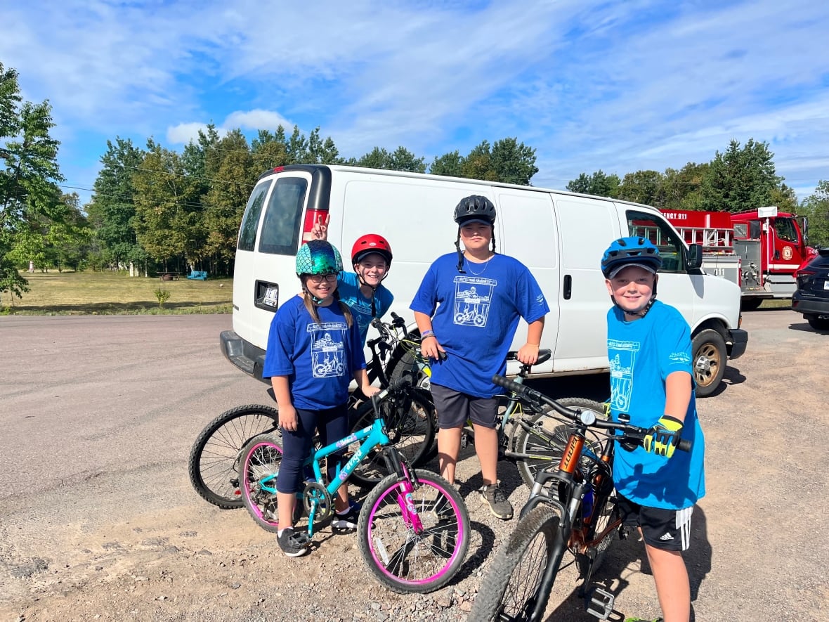 Four kids, three girls and a boy, sit on their bikes on a bright summer day.