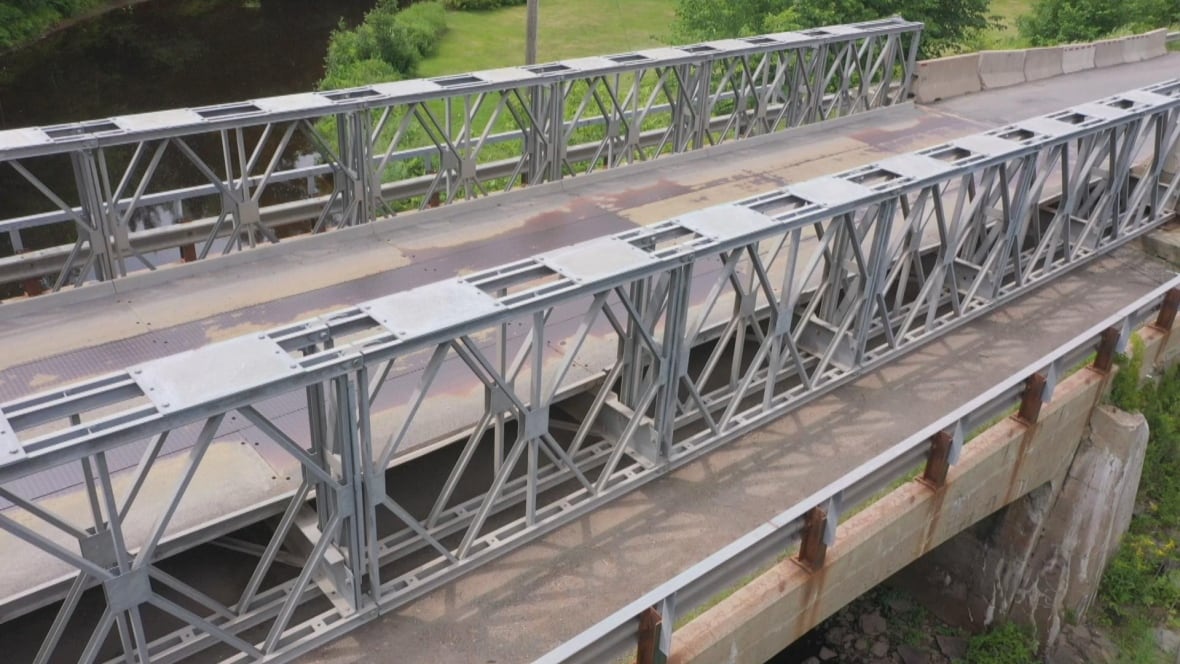 A metal beamed bridge resting overtop a concrete structure bridge overtop of a shallow river.