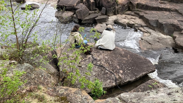 People sitting near some rapids with recording equipment.