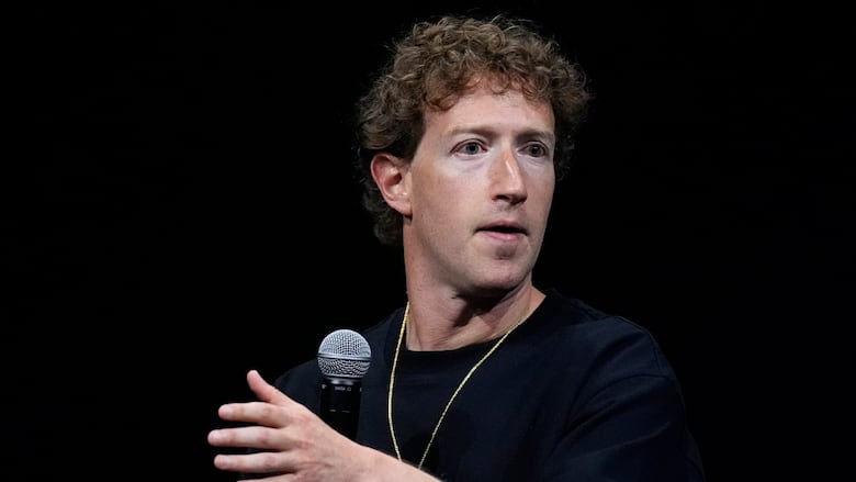 A curly haired cleanshaven man gestures while speaking and seated.