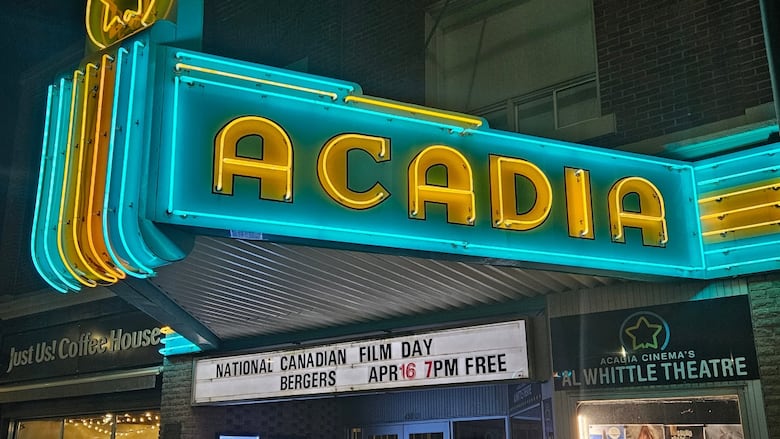 The exterior of a 1920s era movie theatre at night with bright blue and yellow neon.