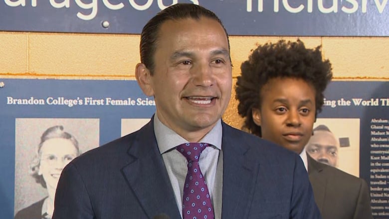 A man stands at a podium with another person standing in the background.