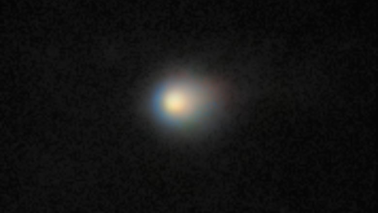 A yellowish fuzzy object sits in a black sky. 