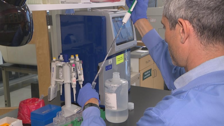 A man in a lab coat dropping liquid into a test tube in a lab.