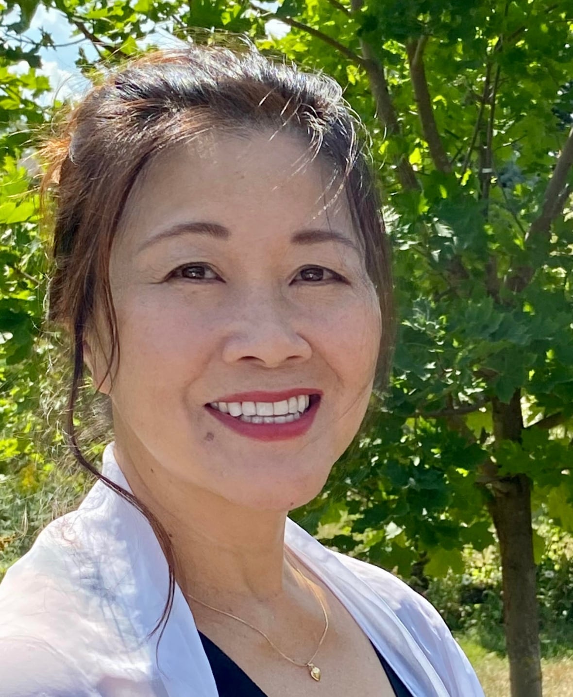 a woman with brown hair and brown eyes wearing a white button down shirt over a black tee shirt smiles