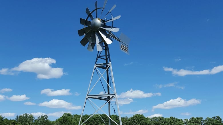 A silver metal windmill seen outside with trees in the background.