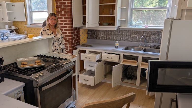 A woman standing in a a disheveled kitchen.