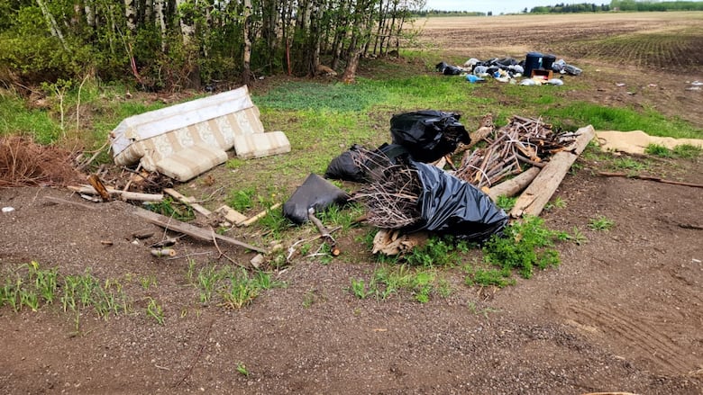 Garbage piles are scattered across a green pasture near a brush of trees next to a family farm in Edmonton, Alberta.