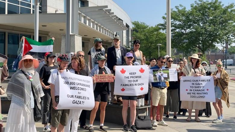 A group of people holding signs and flags pose together in front of an office building.