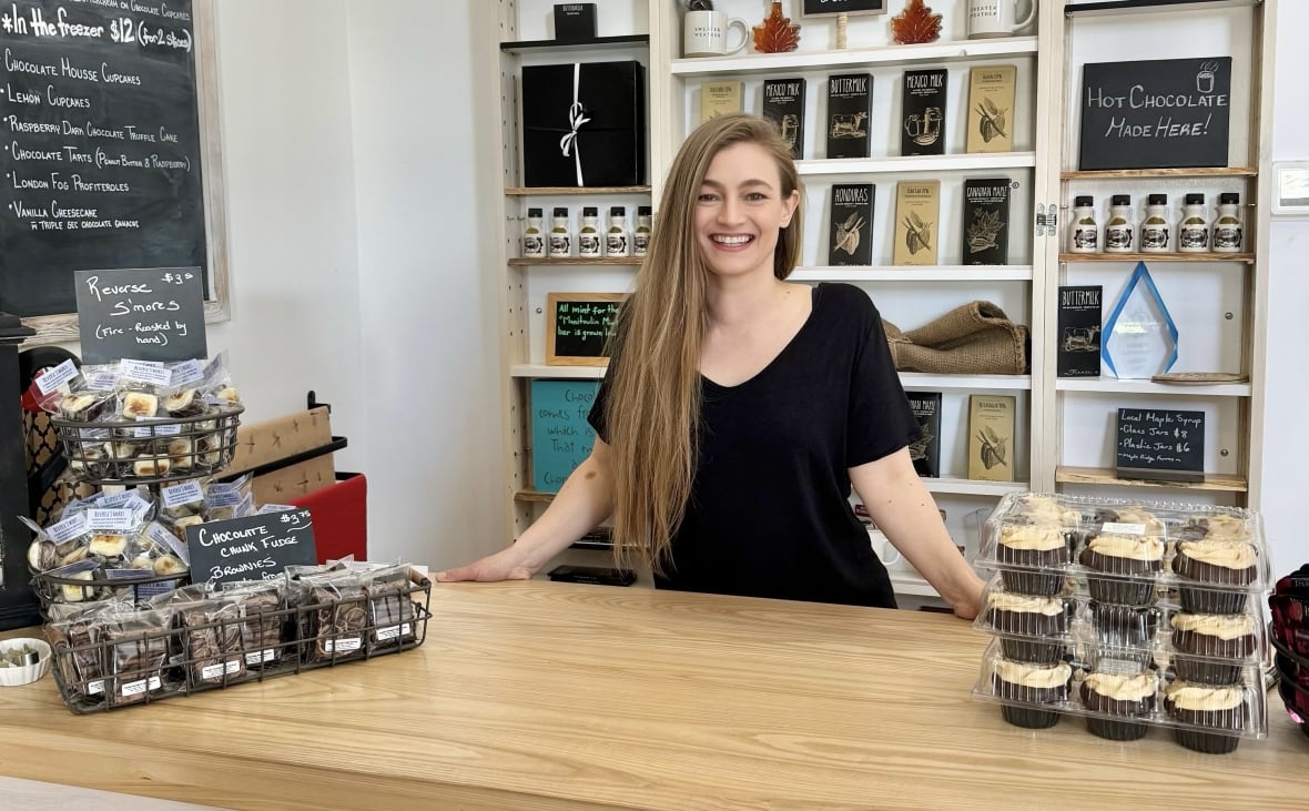 Woman stands behind store counter smiling.