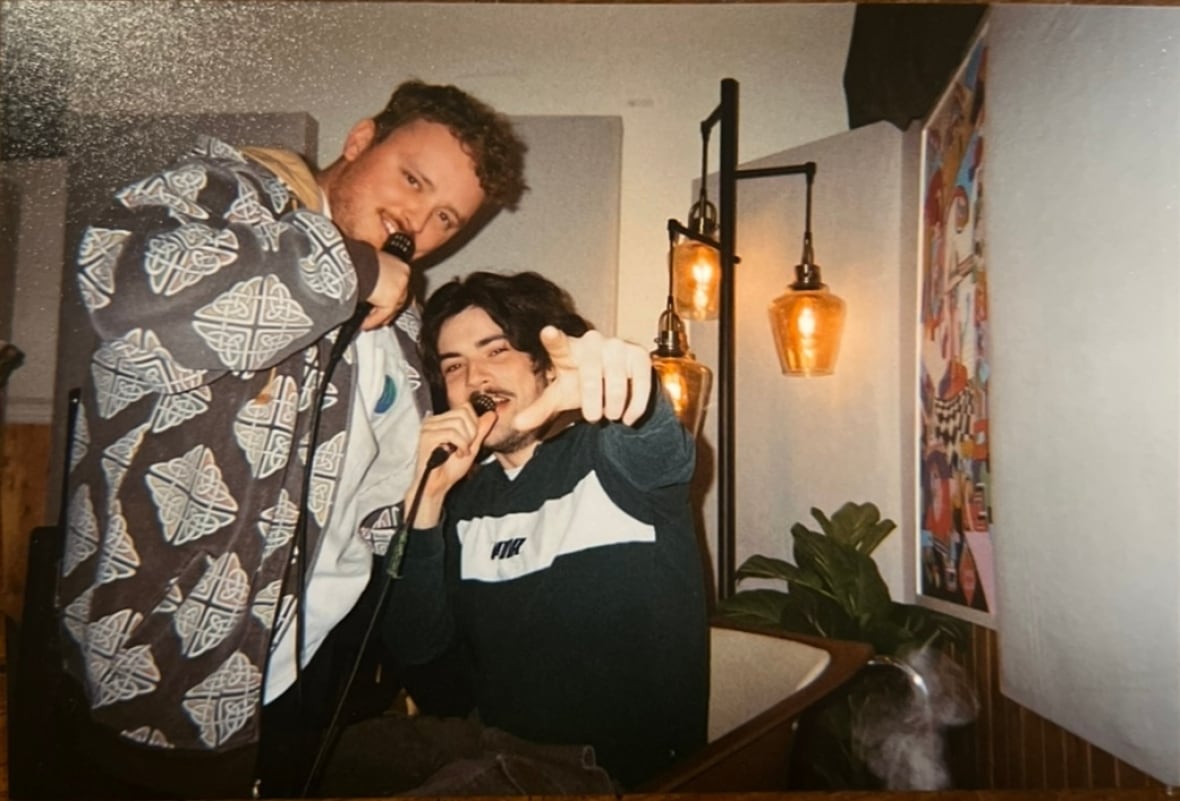Two people in a living room holding microphones and singing while looking at the camera.