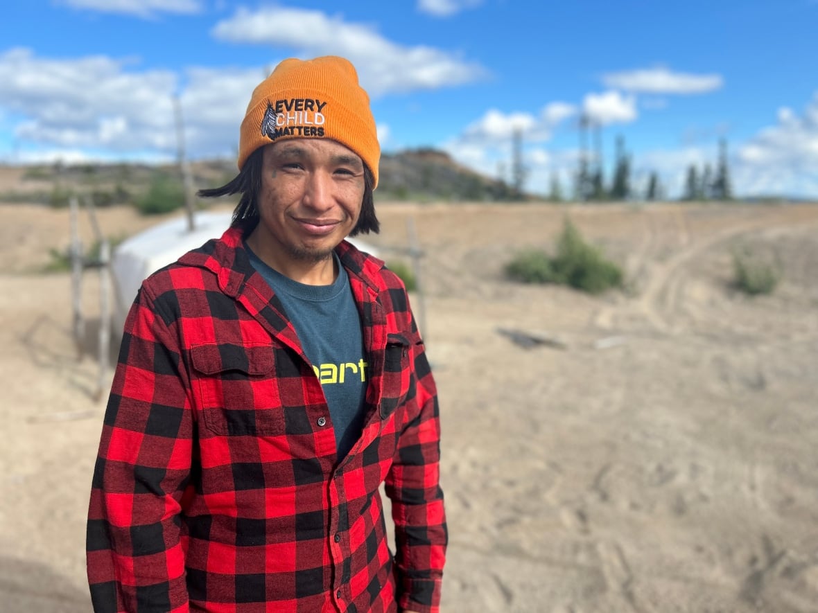 A man in a red coat and orange hat standing outdoors. 