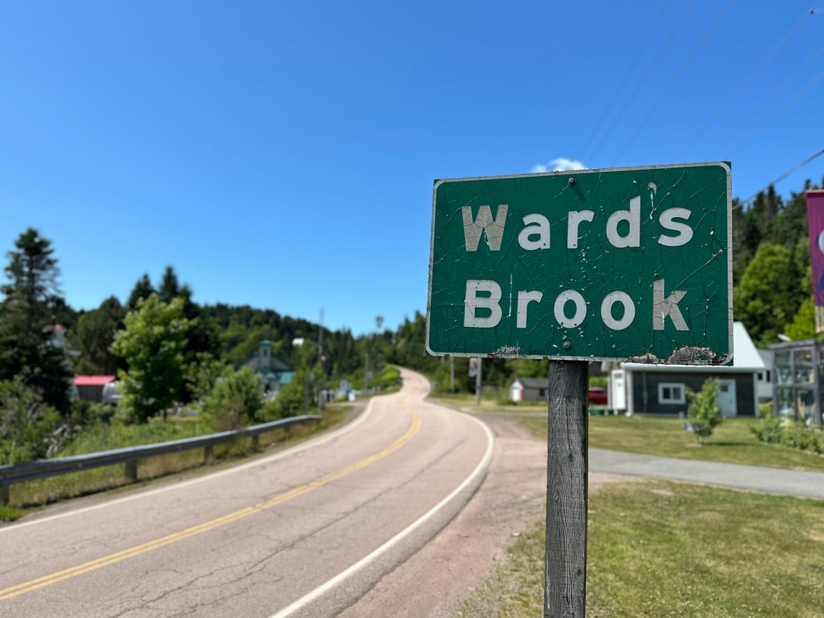 A worn road sign says 'Wards Brook,' and a winding road is seen in the background.