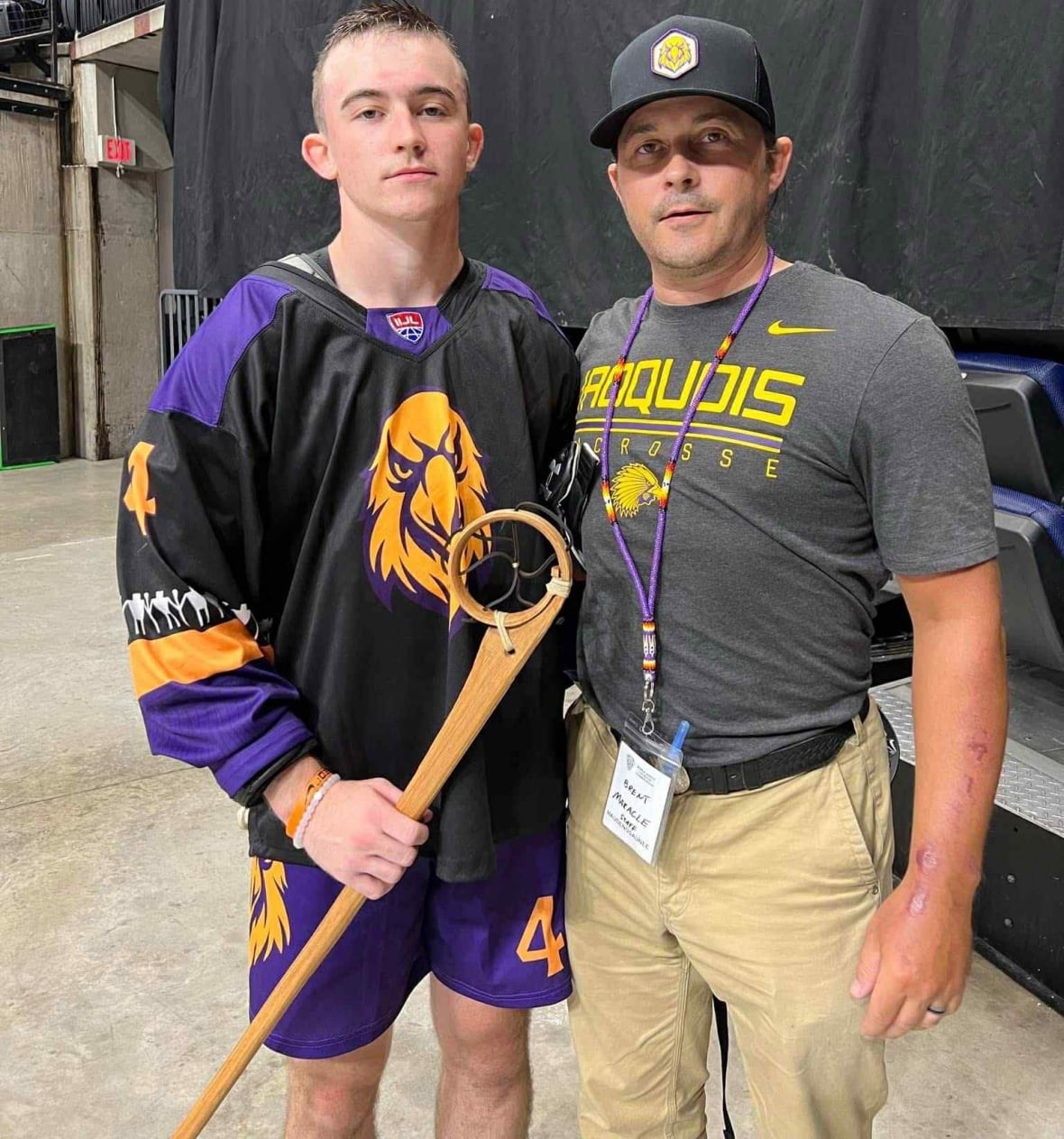 Father and son holding wooden lacrosse stick.