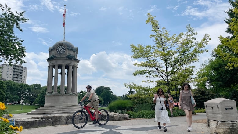 People walk through a park on a summer day with blue skies and some clouds