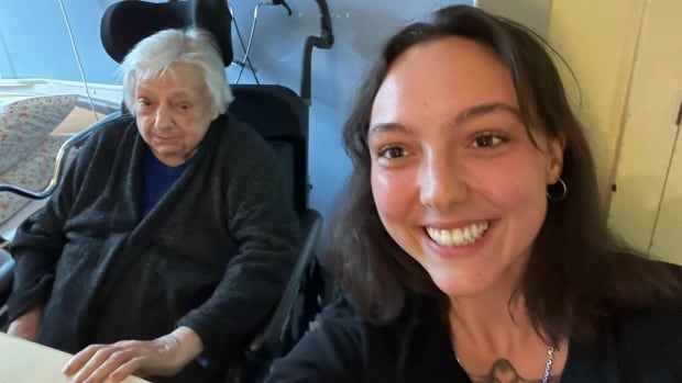 A woman takes a selfie with her grandmother, seated next to her.