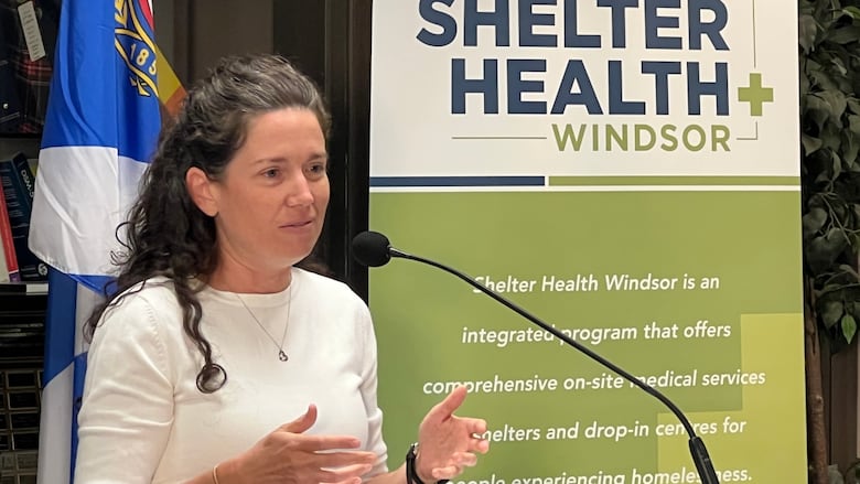 Close-up of Bondy at a podium with a Shelter Health banner behind her. 