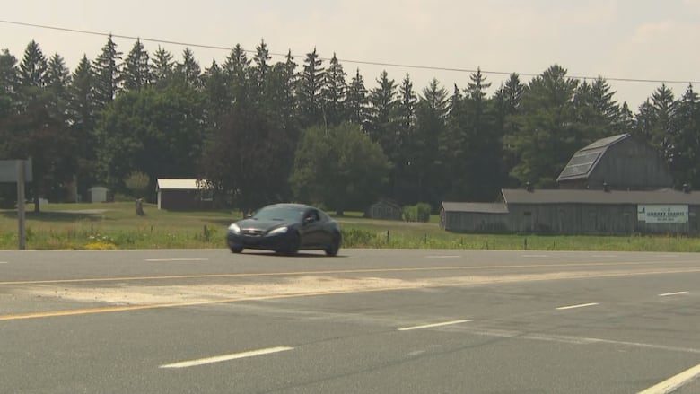 A black car drives on a small stretch of highway with sand in the middle of the road between the lanes.