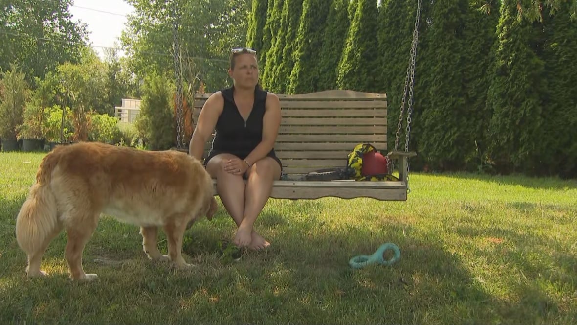 A woman sits on a bench swing while petting her dog. 
