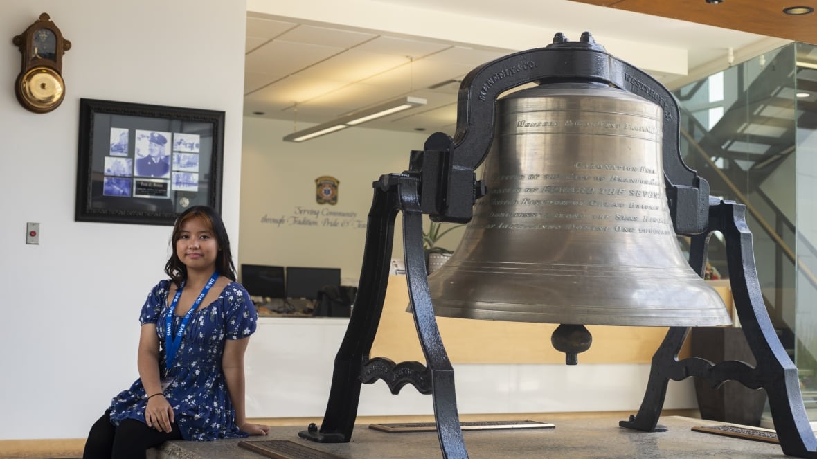 A young woman sits beside a giant fire bell.