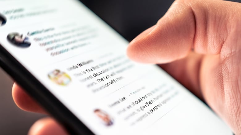 A closeup of a person holding a smartphone with blurred social media posts on the screen.