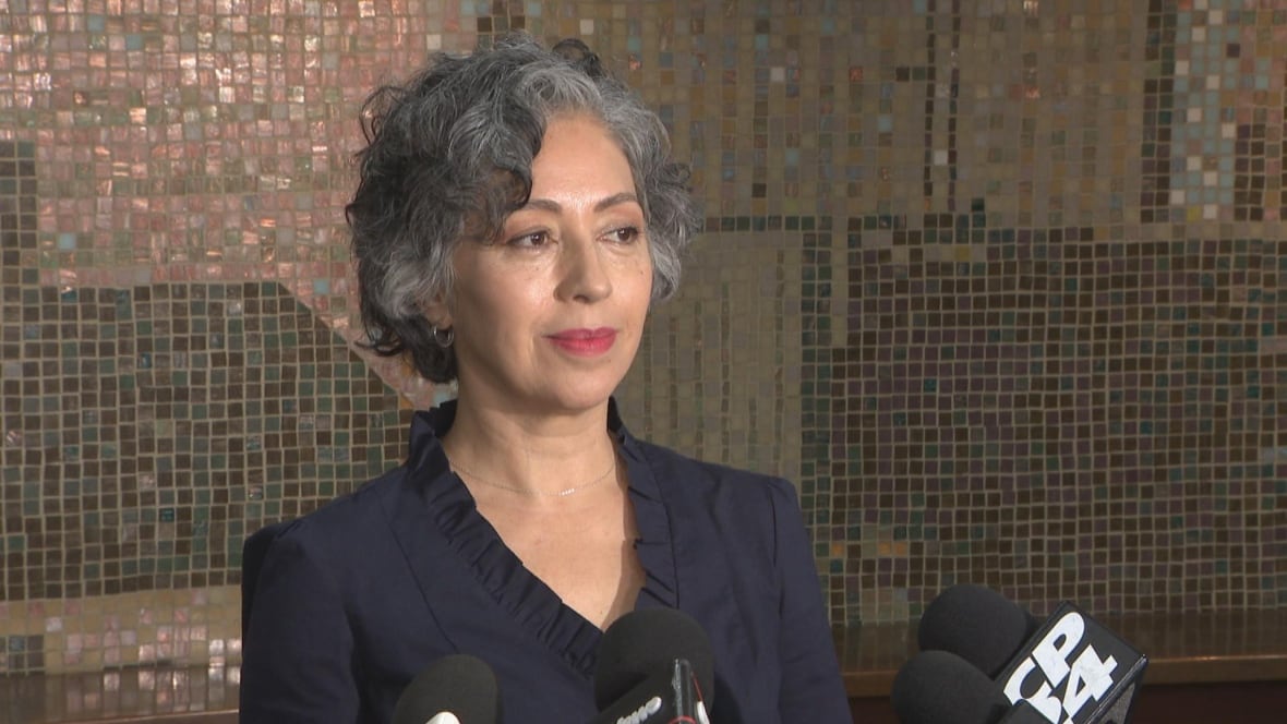 Woman in blue shirt stands in front of microphones smiling