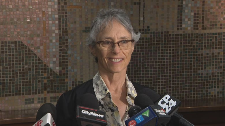 Woman successful  button-up garment  and achromatic  blazer stands successful  beforehand   of microphones, smiling