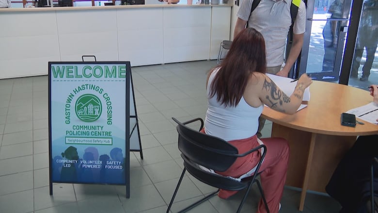 A woman does paperwork at a table next to a sign that says Gastown Hastings Crossing Community Policing Centre.