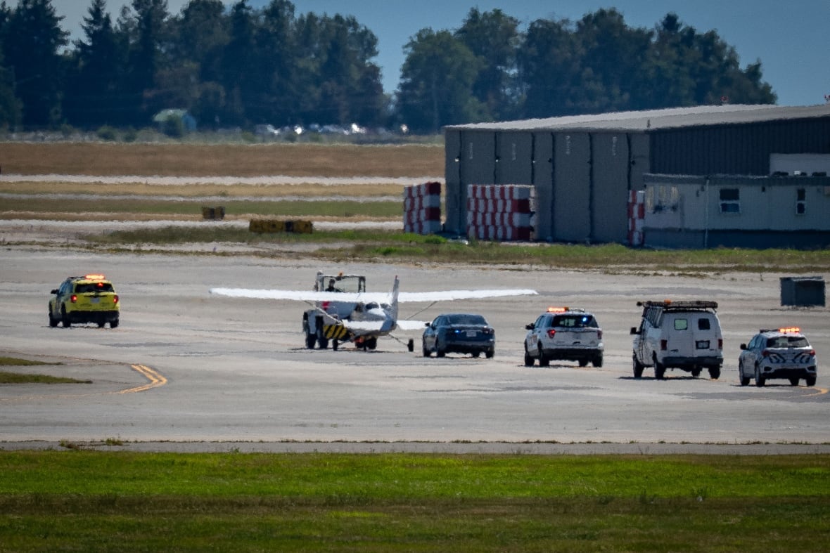 A line of police cars is seen behind a small plane on the tarmac.
