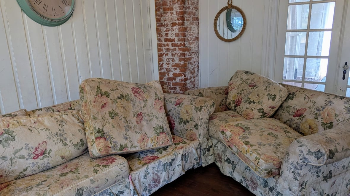 Two couches with brown dirt ground into the white and floral pattern, placed in the corner of a white-walled room.