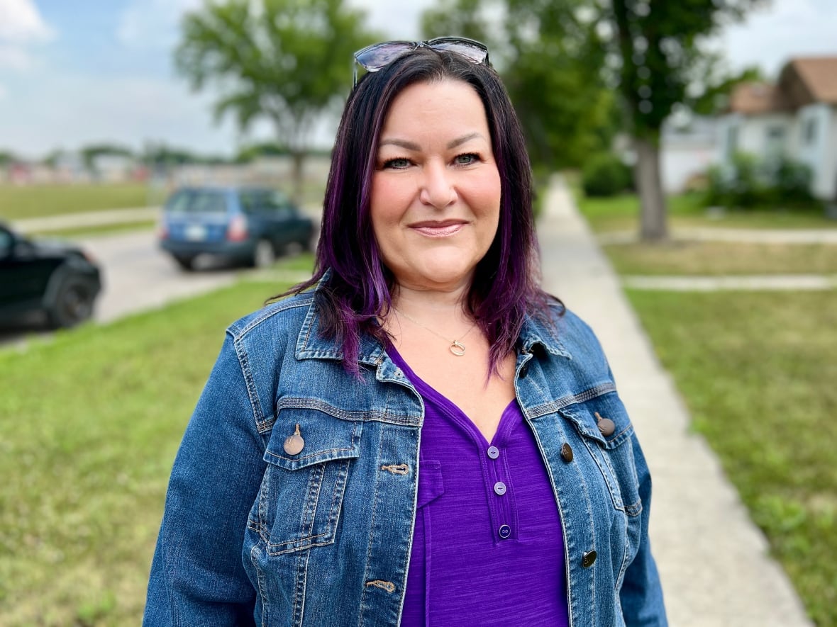 A woman with a purple t-shirt looks at the camera with a smile.