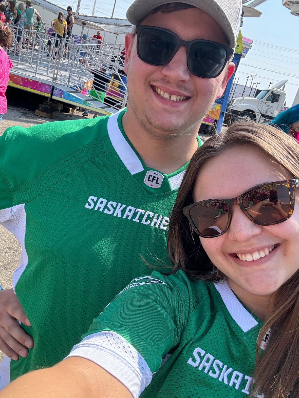A couple in sunglasses and  green Saskatchewan Rougriders jerseys pose for a selfie