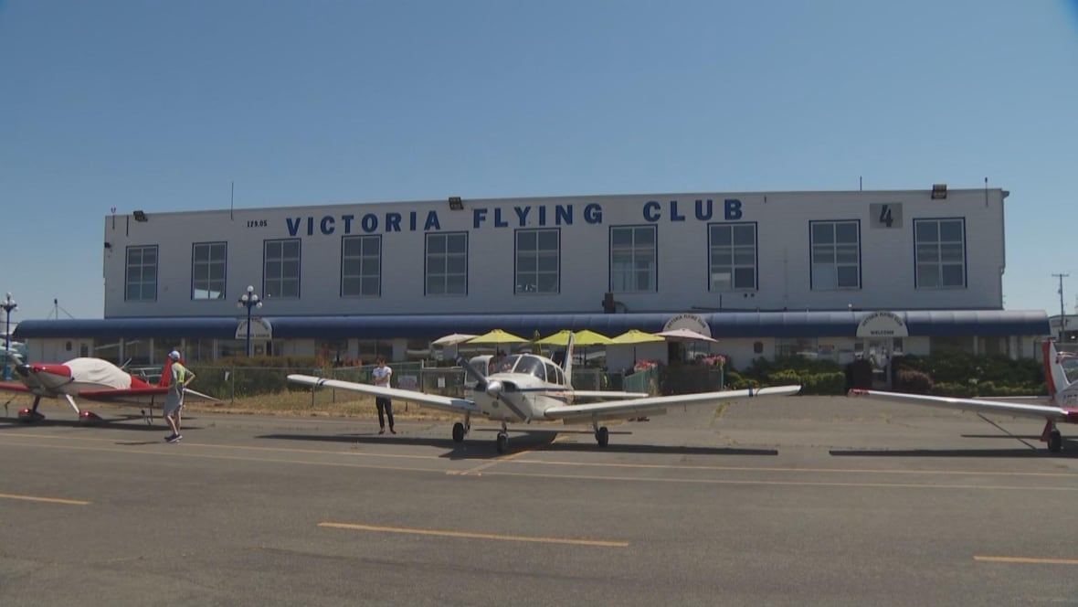 A long building with the name 'Victoria Flying Club' on it and planes outside.