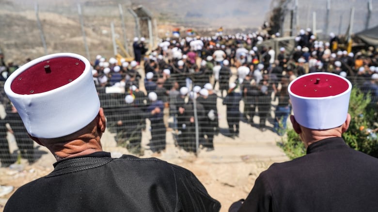 Druze men stand on both sides of the border between Israel and Syria.