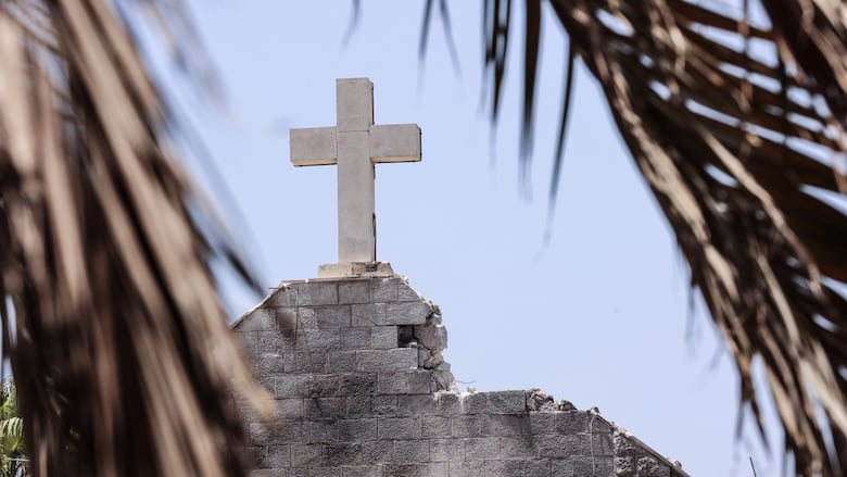 A closeup of a cross atop of a damaged building is shown. 
