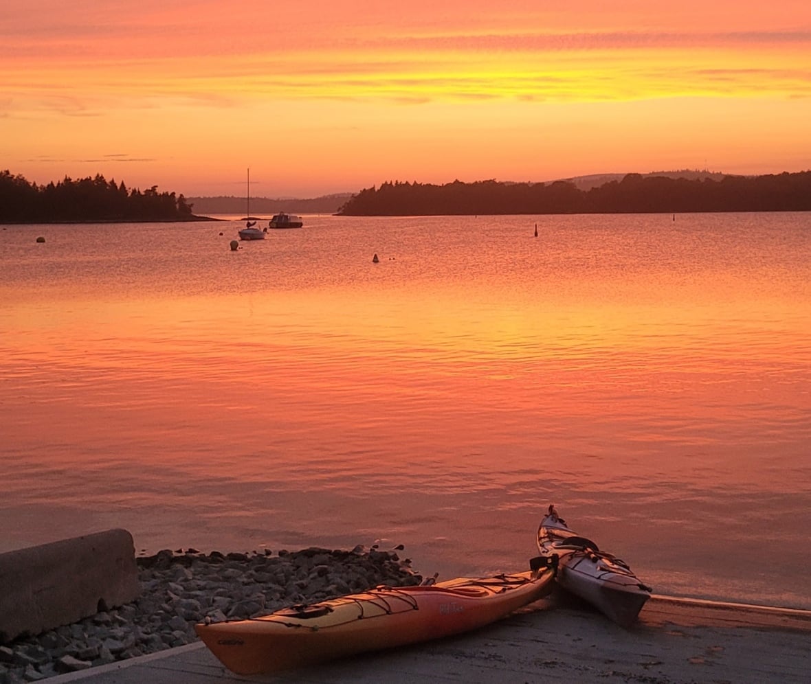 An orange and yellow sunset over the water. Two kayaks are on the boat launch.