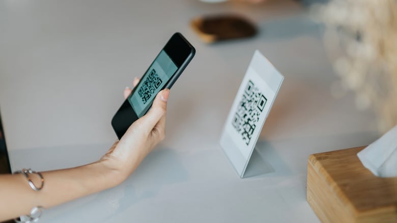 Woman's hand holding smartphone, scanning barcode for contactless payment in the cafe