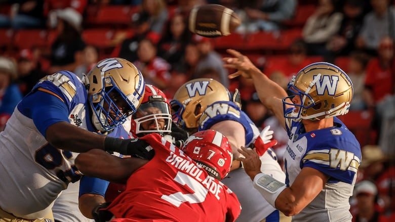 A football quarter back in blue and white throws a ball while teammates try to keep away players in red.