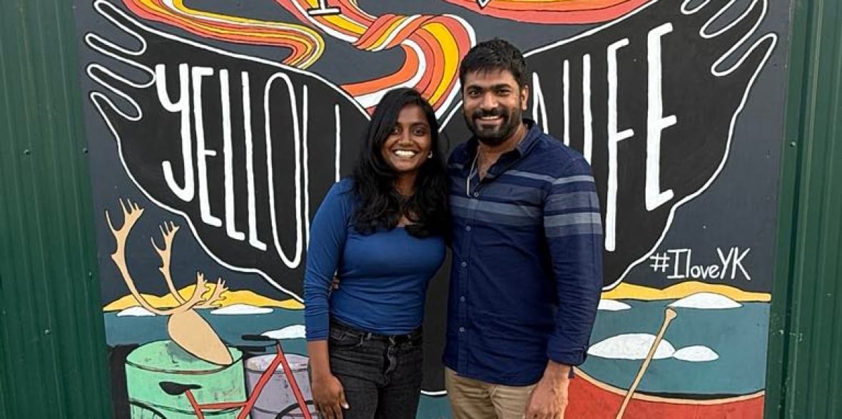 Two people standing next to each other in front of a sign that sign that says 'I love Yellowknife'