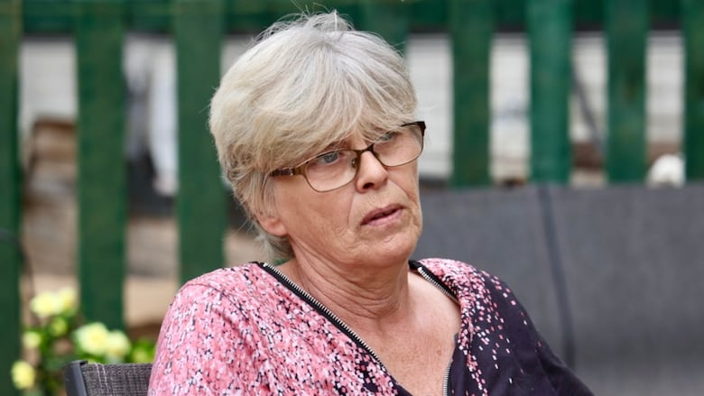 A woman with glasses and short hair speaks to a reporter. 