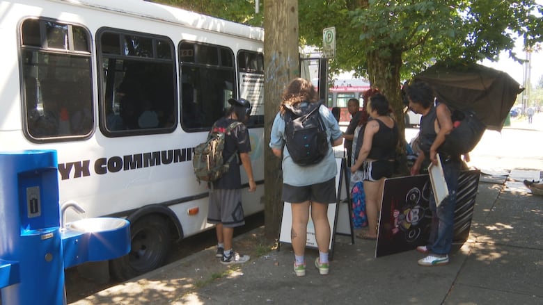 A small group of people gather around the entrance to a white bus, stopped on the side of a street.