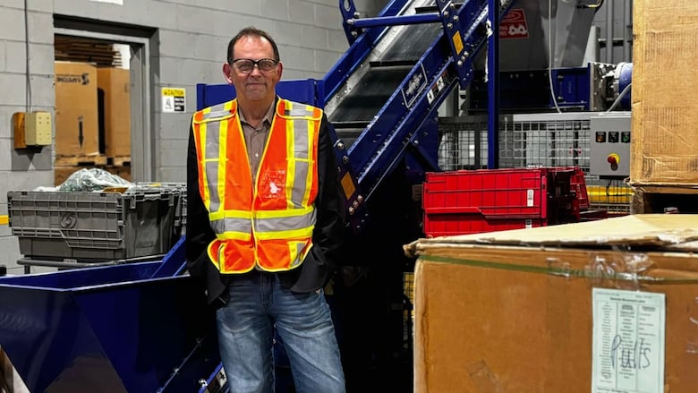 A man stands in front of a shredder surrounded by boxes
