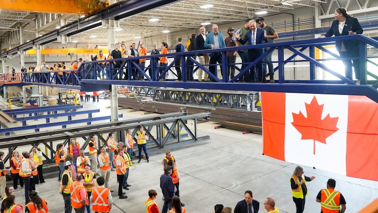 People stand on a bridge in a warehouse overlooking other workers
