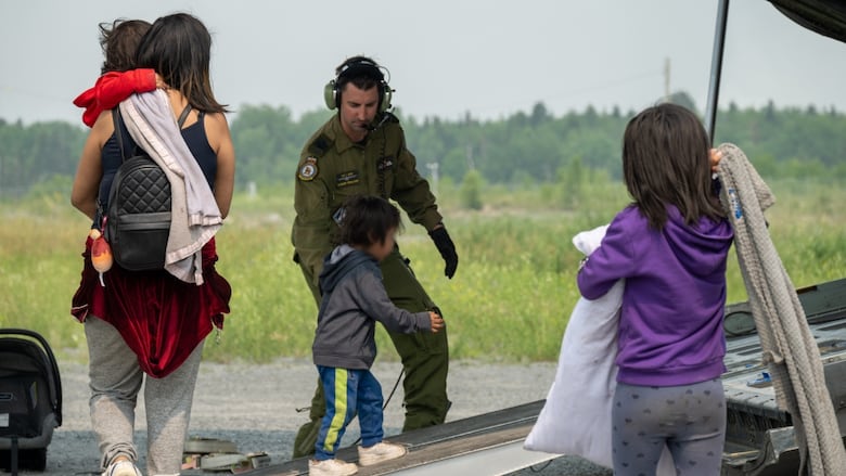 A Canadian Armed Forces member helps a child onto an aircraft.